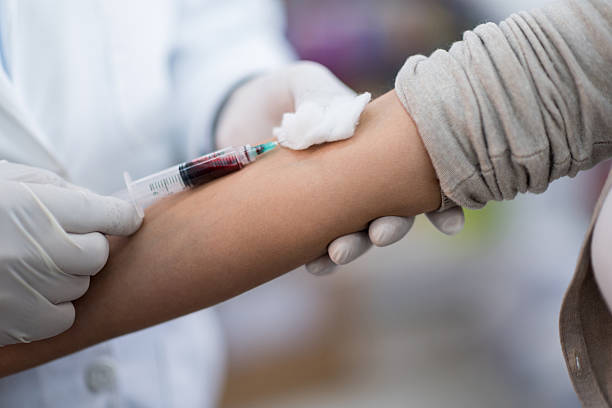 Woman donating blood and doctor holding the needle while it fills