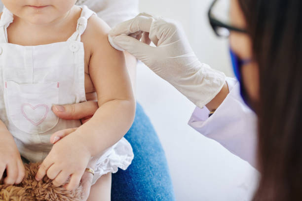 Doctor in rubber gloves wiping injection site on arm of little girl before vaccinate her for coronavirus